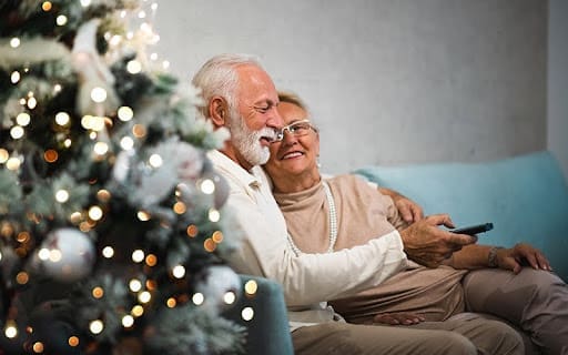 Senior couple cuddling on couch by christmas tree watching christmas movies
