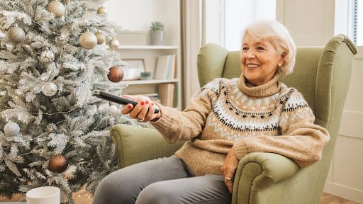 Senior lady turning on tv by christmas tree